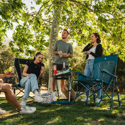 A group of people at a park having snacks while they sit in a Comfort Pro Rocker and a BreezeRocker. 