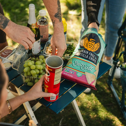 A group of people reaching for snacks positioned on top of a teal Compact Camp Table. 