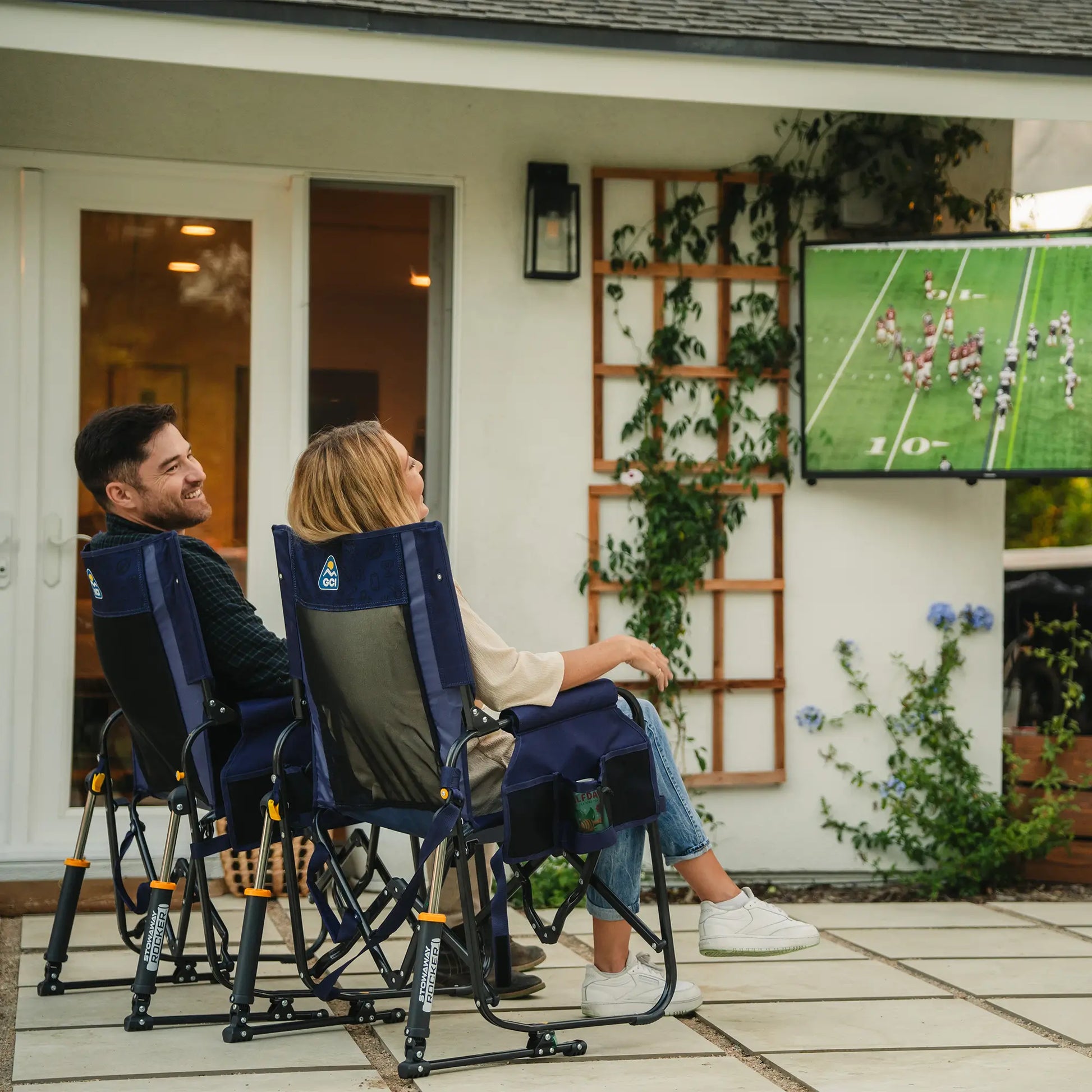 Two people watching a football game on a television while sitting in a tailgater rich blue Stowaway Rocker. 