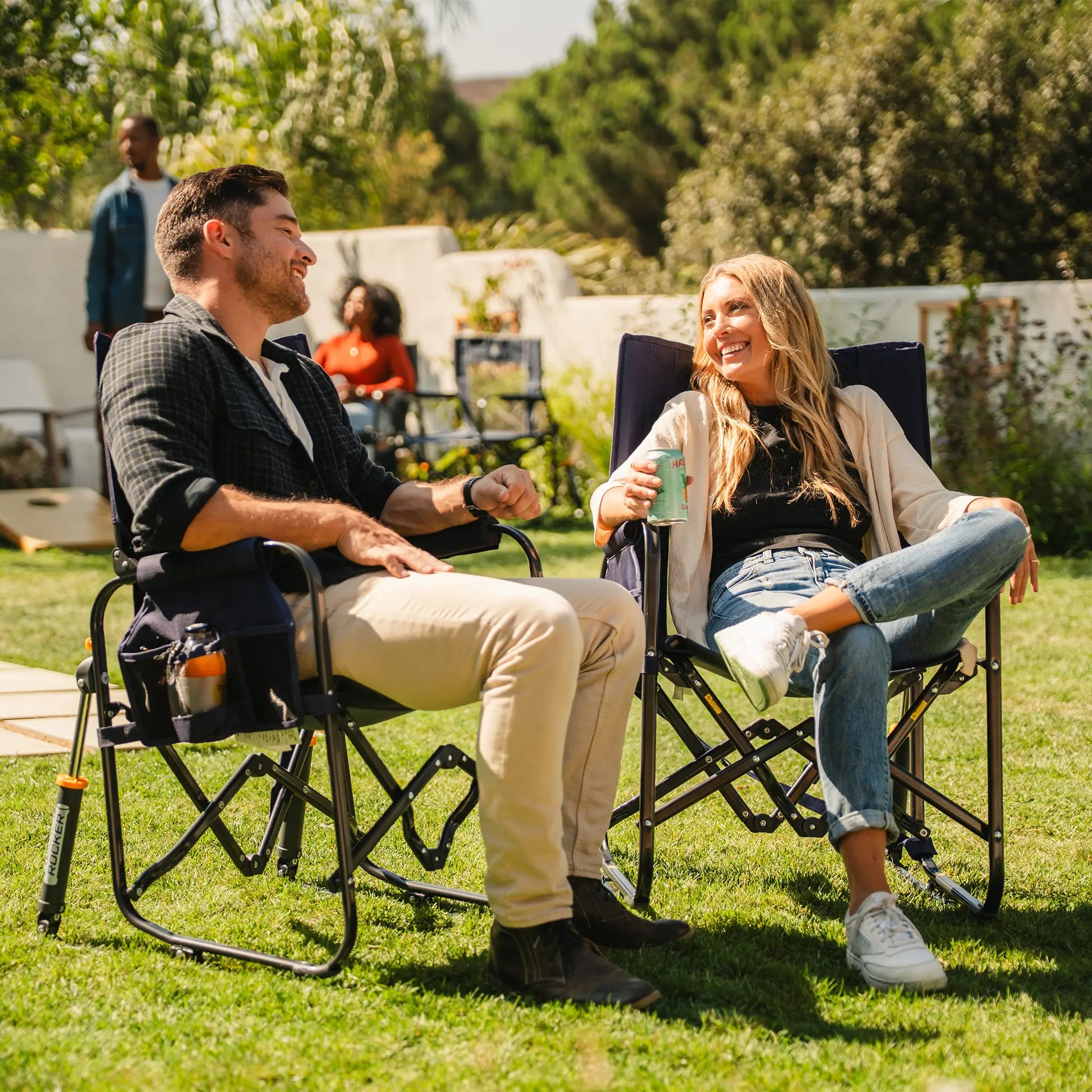 Two people sitting and laughing in a tailgater rich blue Stowaway Rocker in a backyard setting. 